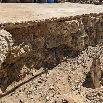 Tom Masonry - Damage inadvertently caused by an excavator with a hammer when breaking through very hard rock to dig a trench for a French drain. - Masonry/Concrete Near Me Tom Masonry - Damage inadvertently caused by an excavator with a hammer when breaking through very hard rock to dig a trench for a French drain. - Masonry/Concrete Near Me
