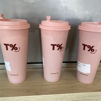 T% Coffee + Tea - Davis  - Three pink T% Coffee + Tea cups with lids are placed on a wooden surface against a metallic background, each with a white label. - Bubble Tea Near Me - Davis, California