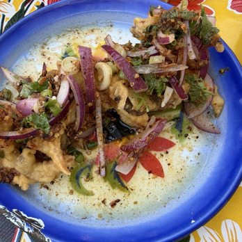 Glai Baan - Tempura Oyster Mushrooms - Fried oyster mushrooms topped with red onions, green onions, and herbs, served on a blue plate with some sauce and seasoning. - Thai Near Me - Phoenix, Arizona