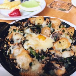 Egg bake - A baked dish featuring melted cheese, greens, and chunks of chicken or vegetables served in a black skillet, with fruit and a drink in the background.