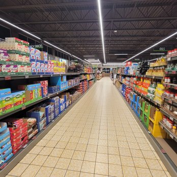 ALDI - Canned - A wide aisle in ALDI grocery store with shelves on both sides filled with snacks, oils, and condiments, illuminated by overhead lighting. - Grocery Near Me - Exton, Pennsylvania
