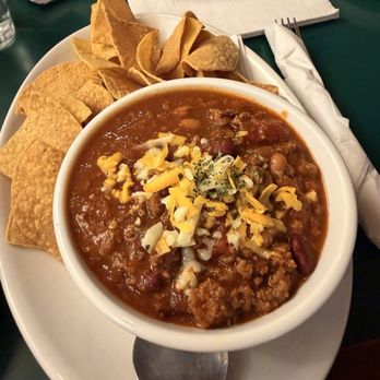 Red Lion - Award-winning Red Lion Red Chili - A bowl of chili with ground meat, beans, and tomato sauce, topped with shredded cheese, served with tortilla chips on a white plate. - Bars Near Me - Vail, Colorado