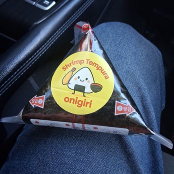 Seoul Gimbap - Instructions are on back. - A shrimp tempura onigiri in clear plastic packaging with a cartoon rice ball label, placed on a person's lap in a car. - Food Delivery Services Near Me - Albuquerque, New Mexico