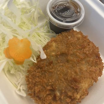 Cafe Oriental - Curry Croquette - A breaded fried cutlet, likely pork or chicken, is presented on a white tray alongside shredded cabbage and a small plastic container of dipping sauce. The cabbage includes a decorative flower-shaped carrot slice. The meal appears to be served in a casual dining setting, possibly a Japanese or Asian-inspired eatery. - Asian Fusion Near Me - Miami, Florida