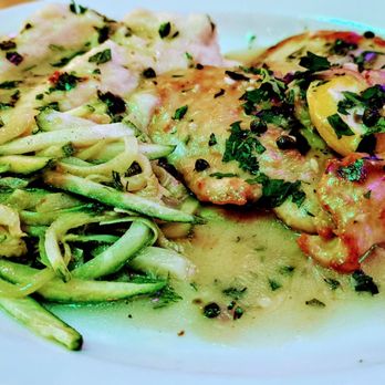 Tune-Up Cafe - Chicken picatta - A dish featuring chicken piccata with a lemon slice on top, covered in a creamy sauce with herbs and black pepper. Accompanying the chicken are pasta with zucchini and a side of additional vegetables, all presented on a white plate. The meal appears to be served in a casual dining setting, highlighting a fusion of flavors. - New Mexican Cuisine Near Me - Santa Fe, New Mexico