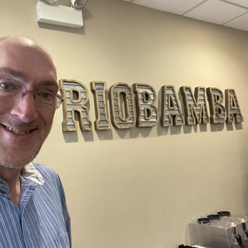 Riobamba - Tasteful, clean decor! - A man wearing glasses and a striped shirt is taking a selfie in front of a wall with a 'RIO BAMBA' sign inside a restaurant. - Tacos Near Me - Glenview, Illinois