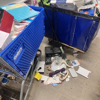 Gabe's - A shopping cart filled with various items, including papers, boxes, and containers, is positioned next to a blue cart with more supplies. Items and debris are scattered on the floor. - Women's Clothing Near Me - Pottstown, Pennsylvania