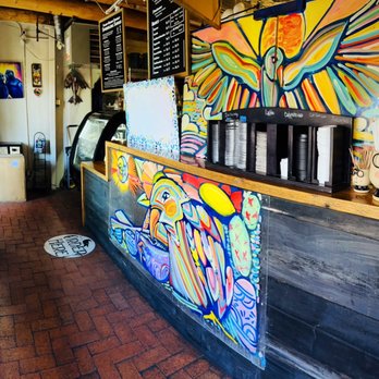 Blackbird Coffee House - Ordering and counter station - The coffee shop features a vibrant mural with abstract and bird motifs behind the counter, with menu boards and coffee accessories visible. - Coffee & Tea Near Me - Albuquerque, New Mexico