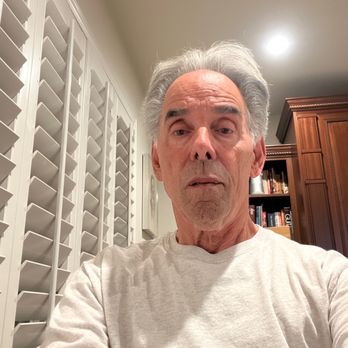 Hear No Evil Studio - An older man with gray hair and a neutral expression is taking a selfie inside a room with white window shutters and a wooden bookshelf. - Recording & Rehearsal Studios Near Me - Orange, California