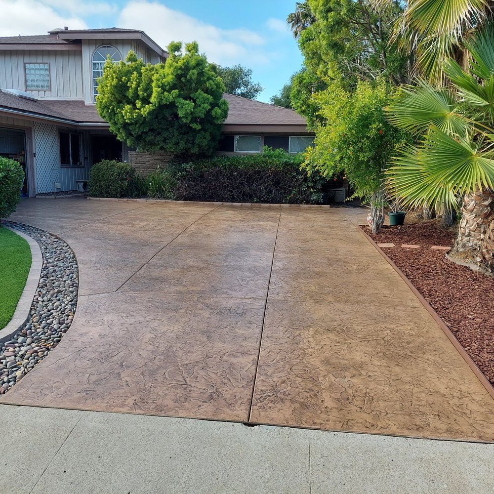 Stamped concrete driveway integrated into existing rock feature on left and accented with new trim on right. Stamped concrete driveway integrated into existing rock feature on left and accented with new trim on right.