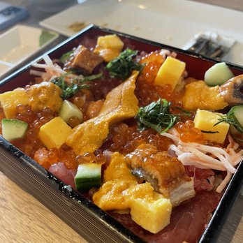 Chicago Sushi - Chirashi-Sushi(jewelry box) - A rectangular sushi jewelry box holds an assortment of sashimi, fish roe, cucumber, tamago, and garnishes. The presentation includes colorful ingredients arranged on a wooden table, with bowls and utensils visible in the background. - Japanese Near Me - Des Plaines, Illinois