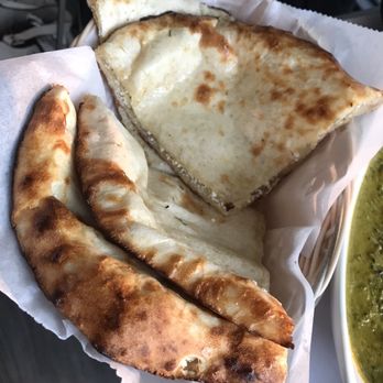 Mint - Indian Lakeside Dining - A basket lined with paper holds Indian flatbreads, including naan and stuffed paratha, which are golden-brown and slightly charred. The naan appears soft with a crispy exterior, while the paratha is thicker and flaky. A side dish, possibly curry or sauce, is partially visible on the right side of the image. The setting suggests a casual dining experience at an Indian restaurant or eatery. - Indian Near Me - Lee, Massachusetts