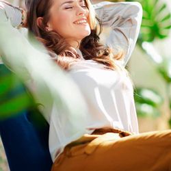 Studio D Brickell - A woman with brown hair and closed eyes smiles as she relaxes in a chair, leaning her head back with her hands behind her hea...