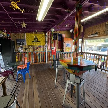 Maggies Shaved Ice - A wooden outdoor seating area with multicolored chairs, American flags, and string lights hanging from the ceiling, decorated with stars and patriotic items. - Shaved Ice Near Me - Cloudcroft, New Mexico