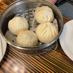 Pork Buns - Four steamed pork buns are placed in a metal steamer basket lined with parchment paper, on a wooden table.