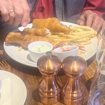 Zut On Fourth - A plate of fish and chips with tartar sauce and ketchup, accompanied by shredded vegetables, on a wooden table. A person is reaching for the food. - Mediterranean Near Me - Berkeley, California