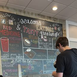 Colorful menu options - A man with dark hair and a black shirt is looking at a large chalkboard menu with colorful writing inside a cafe or restaurant.
