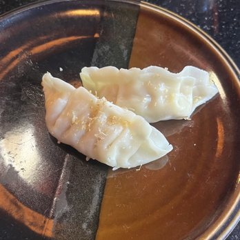 Red 88 - Davis - Chicken Pot Stickers - Two chicken pot stickers are placed on a divided metal plate, with one side of the plate being darker and the other lighter, on a black countertop. - Asian Fusion Near Me - Davis, California