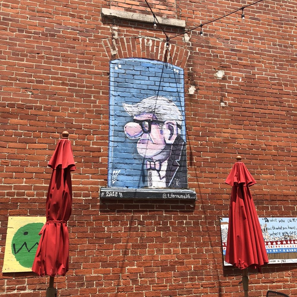 The Alley - a brick wall with a mural of a man with a mustache - American Near Me - Tipton, Indiana