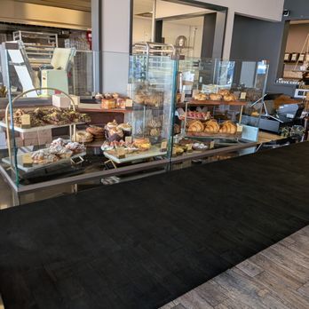 Sucre Table - A bakery counter features an assortment of baked goods including croissants, cookies, and pastries arranged on tiered trays behind a glass display. The interior has a modern design with a dark counter surface, visible kitchen equipment, and shelving with plants and decor. The setup is typical of a contemporary bakery offering takeout options. - Bakeries Near Me - Tampa, Florida