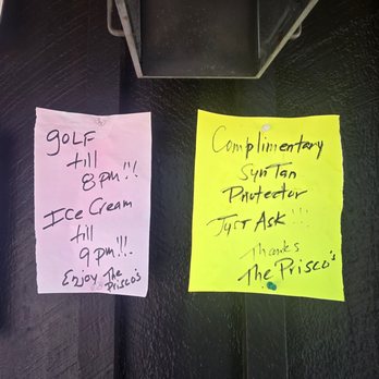 Prisco's - A pink note and a yellow note are taped to a dark, textured surface, positioned near a small, metallic display case. The pink note states that the business offers golf and ice cream until 8 pm and 9 pm respectively, with a message to enjoy the Prisco's. The yellow note mentions complimentary sunscreen and a request to ask for assistance, ending with thanks to The Prisco's. Both notes are handwritten with casual, informal script and are secured with push pins. - Delis Near Me - Bridgewater, Massachusetts