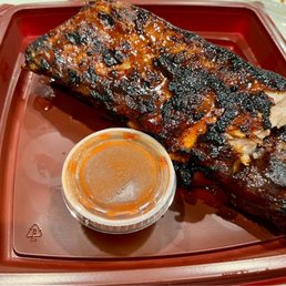 Full Rack of Baby Back Ribs in take out container with a small side of extra BBQ sauce Full Rack of Baby Back Ribs in take out container with a small side of extra BBQ sauce