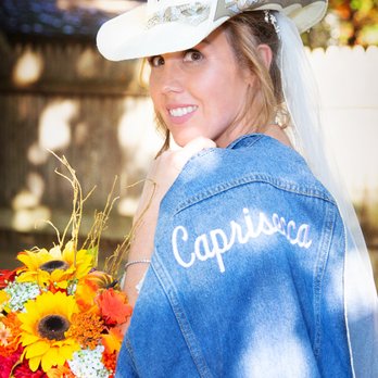 Storm Photographers - Portrait of the Bride wearing cowgirl hat with denim jacket over her shoulder during her back yard horse stable wedding. - Event Photography Near Me