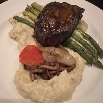Artisan - Filet - A plated meal includes a cooked beef filet with a glaze, green asparagus spears, mashed potatoes topped with sautéed mushrooms and a tomato slice, all arranged on a white plate. The presentation emphasizes the variety of ingredients and textures. - French Near Me - Elkhart, Indiana