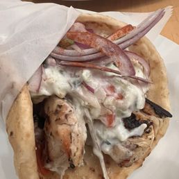 Chicken souvlaki with slivered onions thin sliced tomato and taziki sauce in a pita.