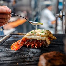 Truluck's Ocean's Finest Seafood & Crab - a cold water lobster tail being finished on the broiler with melted butter being drizzled over the top with a spoon
