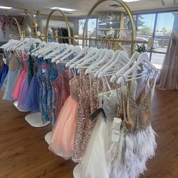 Mayfair Dresses - A clothing rack with various formal dresses, including prom and evening gowns, is inside a boutique with large windows and mannequins. - Sewing & Alterations Near Me - Phoenix, Arizona