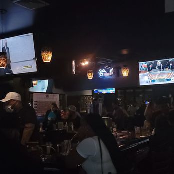 The Draft - A dark interior of a sports bar with several TV screens displaying sports programs and a crowd of patrons gathered around tables. - Pubs Near Me - Allston, Massachusetts