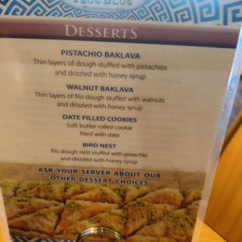 True Blue - The image shows a dessert menu from True Blue Mediterranean Grill, featuring options such as pistachio baklava, walnut baklava, date-filled cookies, and bird nest. Each dessert is described with details about ingredients like filo dough, pistachios, walnuts, honey syrup, and date filling. The menu encourages asking the server about other dessert choices and includes a photograph of assorted desserts at the bottom. The menu is presented in a clear, organized format with a decorative blue and white border at the top. - Coffee & Tea Near Me - Emmaus, Pennsylvania