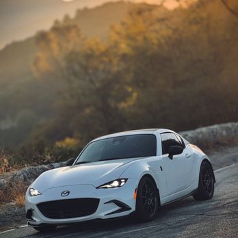 AcutintPro - A white Mazda MX-5 Miata is parked on a mountain road during sunset, with a blurred background of trees and mountains. - Car Window Tinting Near Me - Upland, California