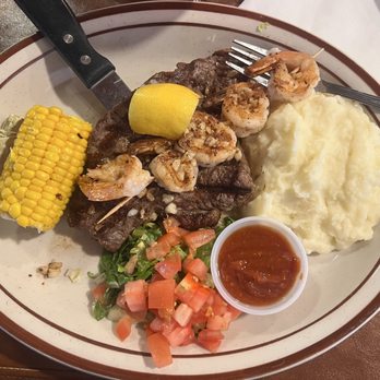 Casa De Valdez - Steak and grilled shrimp with corn on cob and mashed potatoes - A meal featuring steak with grilled shrimp, mashed potatoes, corn on the cob, a small side salad, and a cup of sauce, served on a large oval plate. - Barbeque Near Me - Taos, New Mexico