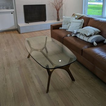 Rhema Construct - floors! - A living room features a glass coffee table, a brown leather sofa with decorative pillows, and a window with a view of trees and grass. - Flooring Near Me