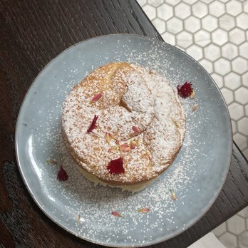 Sudova * Eastern European Kitchen - A round dessert with powdered sugar and flower petals on a gray plate, placed on a dark wooden table. - Modern European Near Me - Cincinnati, Ohio
