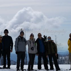Big Trees Tours - Seven friends dressed for cold weather stand in front of a cloudy mountain view.
