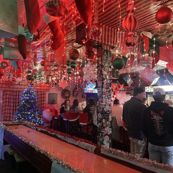 River - A bar interior decorated for Christmas with hanging stockings, ornaments, and a lit Christmas tree, with patrons seated at the bar and standing. - Bars Near Me - Denver, Colorado