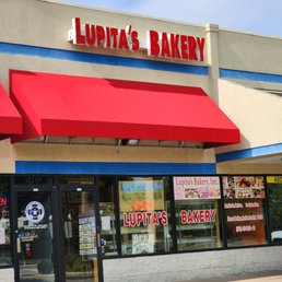 the outside of the store - Lupita's Bakery storefront features large glass windows, red awnings, and signage displaying the bakery's name and opening hours.