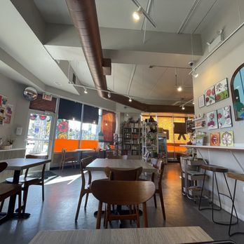 Khepri Cafe - A café interior features wooden tables and chairs, artwork on the walls, and large windows allowing natural light to enter. - Cafes Near Me - Chicago, Illinois