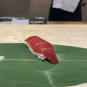 Roji - A single piece of tuna nigiri sushi placed on a green leaf, with a wooden surface underneath, in a sushi restaurant setting. - Sushi Bars Near Me - Cincinnati, Ohio