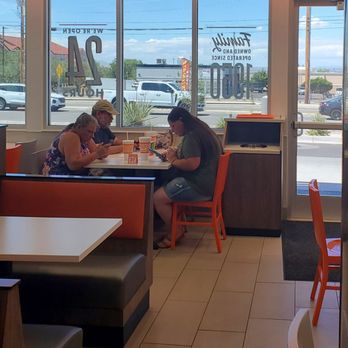 Whataburger - Seating - Inside Whataburger, three customers sit at a table near large windows, engaged with their phones, with a parking lot visible outside. - Burgers Near Me - Albuquerque, New Mexico