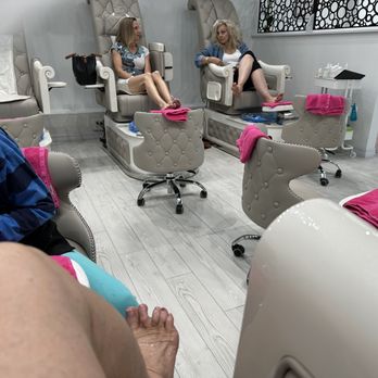 Queen Nails - Bowls are lined and tools are sterilized and wrapped for each new client. - Two women are seated in pedicure chairs at a nail salon, with their feet in the chairs. The salon features multiple pedicure stations with sterilized tools wrapped for each client. Towels are placed on the chairs and nearby surfaces. The environment appears clean and organized, with additional salon equipment and supplies visible in the background. - Nail Salons Near Me - St. Augustine, Florida