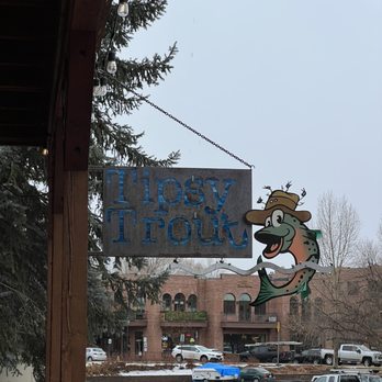 The Tipsy Trout - Outside - A sign for Tiosy Trout with a cartoon fish wearing a hat is displayed outside, with a parking lot and buildings in the background. - American Near Me - Basalt, Colorado