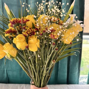 Produce Junction - Beautiful flowers for a customer! - A person holds a large bouquet of yellow roses, multicolored chrysanthemums, and white baby's breath flowers, with a green curtain and window in the background. - Fruits & Veggies Near Me - Exton, Pennsylvania
