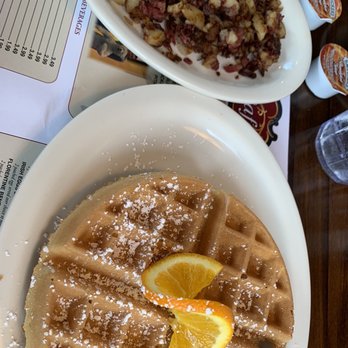 Union Cafe - Waffles w corned beef hash - A plate of Belgian waffles dusted with powdered sugar and garnished with orange slices, accompanied by a bowl of hash with corned beef and potatoes. - Diners Near Me - Schenectady, New York