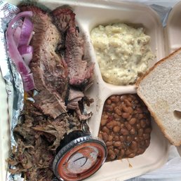 HUGE..Two meat platter. Brisket and pork. - A takeout meal in a compartmentalized container includes sliced beef, baked beans, potato salad, a slice of bread, and onions.
