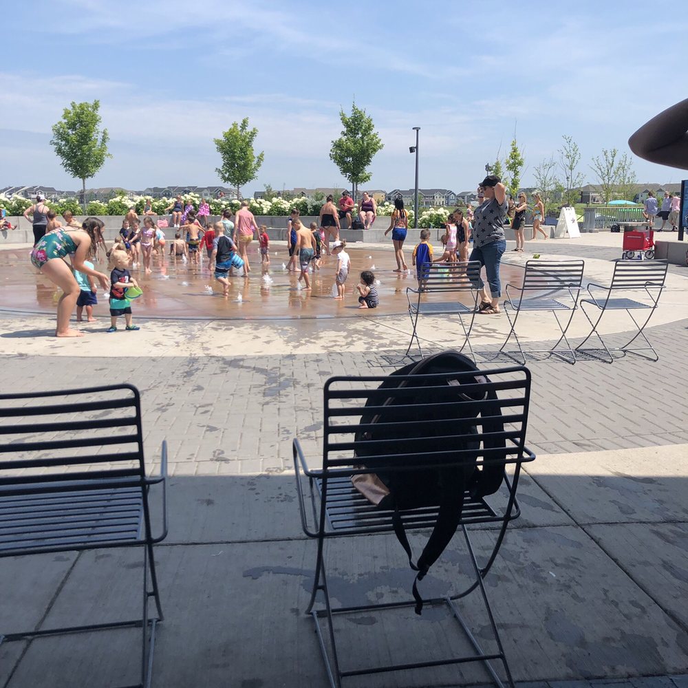 Busy and packed splash pad, people hog chairs they aren't using.