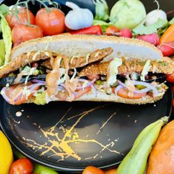 Mesubbim Express - Za'atar Schnitzel on a white baguette layered on a bed of fresh veggies and drizzled with our famous Pesto Aioli and Creamy BBQ sauce